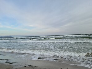 Een strand met golven en een bergketen in de verte.