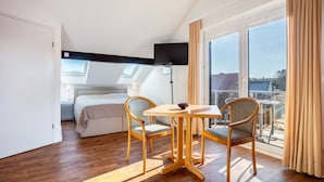 Une chambre d’hôtel avec un lit, une télévision, une table, deux chaises et de grandes fenêtres.