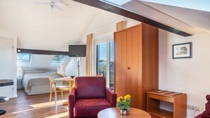 Une chambre moderne avec un fauteuil rouge, une table en bois ornée d’un vase de fleurs, un lit avec vue et une grande armoire.
