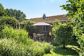 Un jardin avec une table et des chaises, entouré de verdure et bordé d’un bâtiment doté d’un toit en pente.