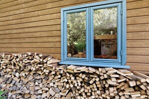 A wooden cabin with a window reflecting trees and a pile of firewood outside. - Holiday Home 'Dollrott' with Private Terrace, Private Garden and Wi-Fi (Süderbrarup)