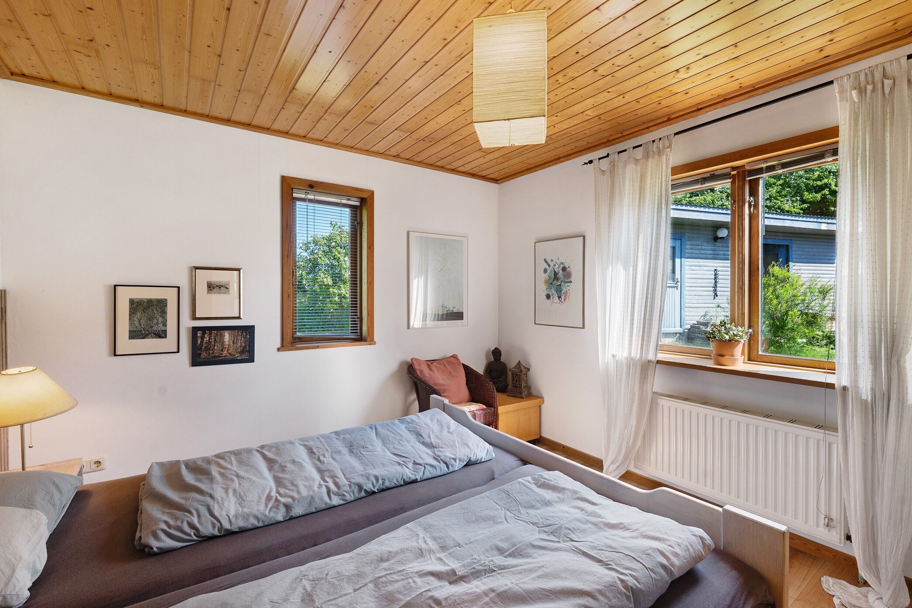 Una camera da letto con un letto, una finestra con tende, un termosifone e quadri appesi al muro.
