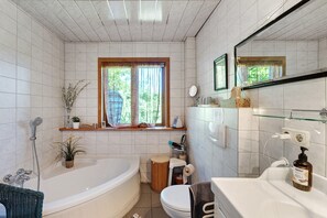 A bathroom with a bathtub, toilet, sink, and a window with curtains.