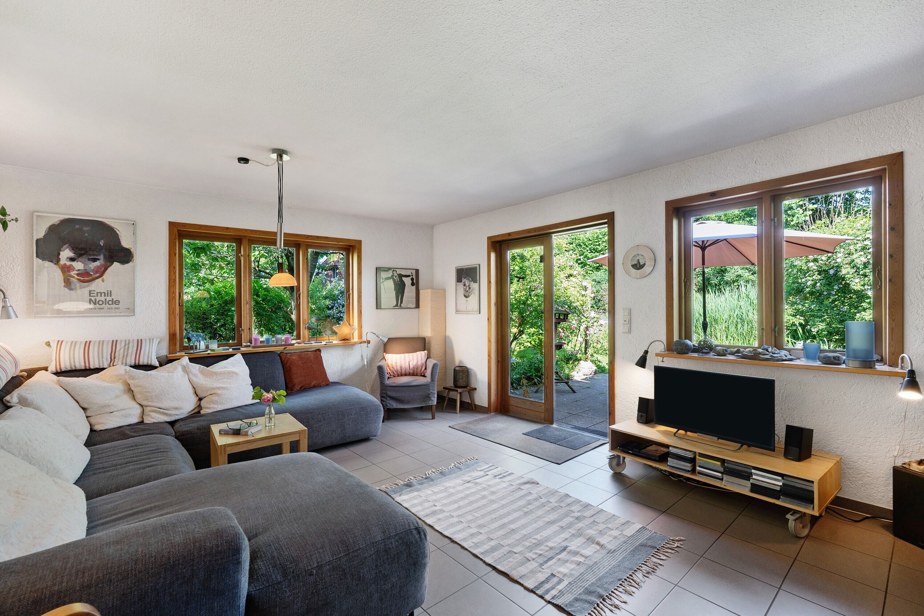 Ein Wohnzimmer mit Sofa, Sessel, Fernseher und Bücherregal.