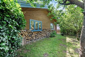 Une cabane en bois avec des fenêtres à cadre bleu, un mur en pierre et une cour couverte d’herbe.