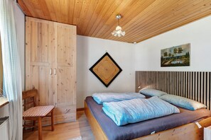 Une chambre avec un plafond en bois, un lit avec une literie bleue, une armoire en bois, un bureau avec une chaise et un tableau accroché au mur.