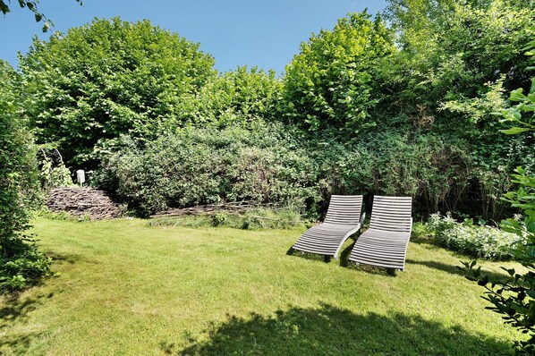 Un espace extérieur verdoyant avec deux chaises longues en bois et une végétation luxuriante en arrière-plan.