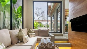 A modern living room with a sofa, a small round table with towels, and a TV mounted on the wall. - Nanna Villa Unit 1 by Betterplace (Canggu)
