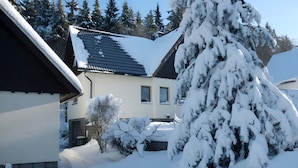 A snow-covered residential area with houses, a tree, and a clear sky.