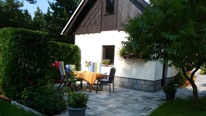 A patio area with a table and chairs, a small window, and potted plants.