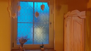 Ein Zimmer mit Fenster, das ein geometrisches Muster zeigt, einem Holzschrank und einer Pendelleuchte.