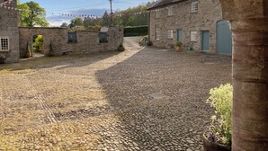 A cobblestone courtyard with stone buildings, a stone archway, and a blue door. - Glanhenwye Courtyard Cottages (Hereford)