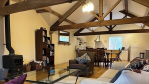 A living room with a glass coffee table, sofas, a fireplace, a bookshelf, and a kitchen area with a dining table and chairs. - Glanhenwye Courtyard Cottages (Hereford)