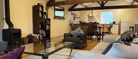 A living room with a glass coffee table, sofas, a fireplace, a bookshelf, and a kitchen area with a dining table and chairs.