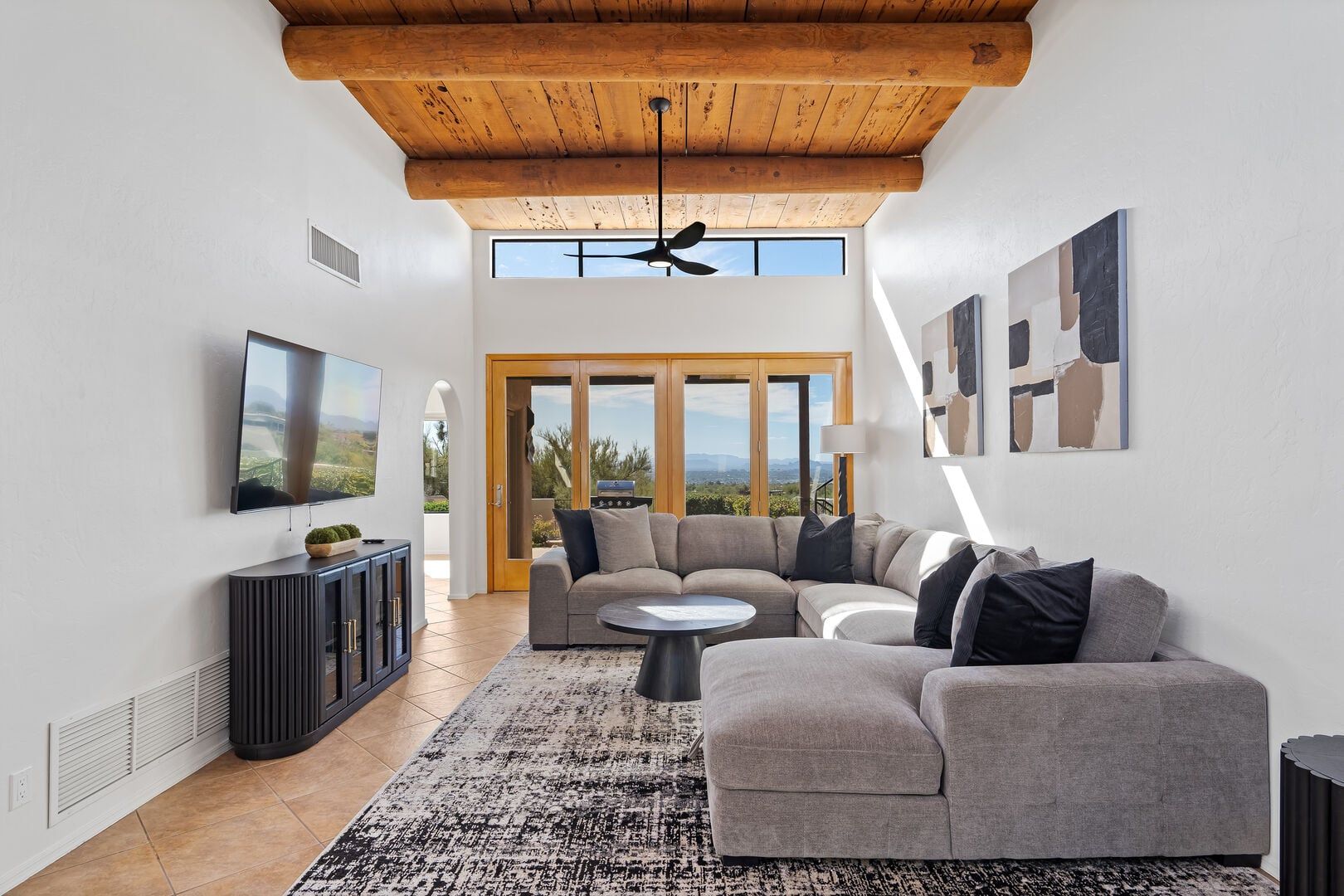 A modern living room with a sectional sofa, a flat-screen TV, and a ceiling fan.
