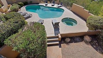 Una piscina con un jacuzzi, rodeada de sillas de descanso y una pequeña escalera de acceso al área de la piscina.