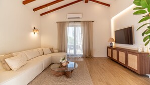 A living room with a sofa, a glass coffee table, a TV on a wooden cabinet, and an air conditioning unit on the wall. - Villa Lere by Villas Guide (Ližnjan)