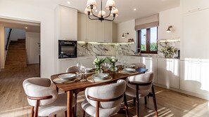 Eine moderne Küche mit weißen Schränken, einer Marmor-Spritzschutzleiste und einem Essbereich mit einem Holztisch, gedeckt für sechs Personen.