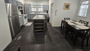 A kitchen with a central island, dark tiled floor, and a dining area with wooden chairs and a table.