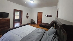 A bedroom with a bed, dresser, television, and a door leading to another room.