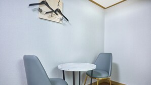 Habitación de esquina con dos sillas grises, una pequeña mesa blanca y una obra de arte colgada en la pared.