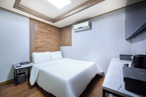 Une chambre d’hôtel comprenant un lit, un bureau, une poubelle, un appareil de climatisation et un mur décoratif en bois.