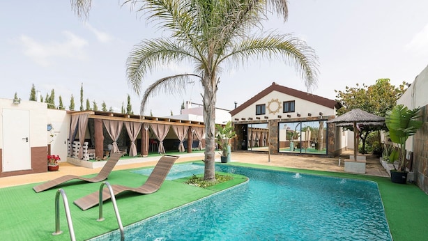 A swimming pool with a palm tree, a covered seating area, and a building with a circular window. - Casa Amelie - Villa With Private Pool. Free Wifi (, Cádiz)