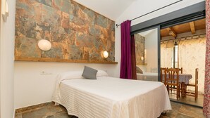 A bedroom with a bed, a stone wall, a wooden ceiling, and a dining area with a table and chairs. - Casa Amelie - Villa With Private Pool. Free Wifi (, Cádiz)