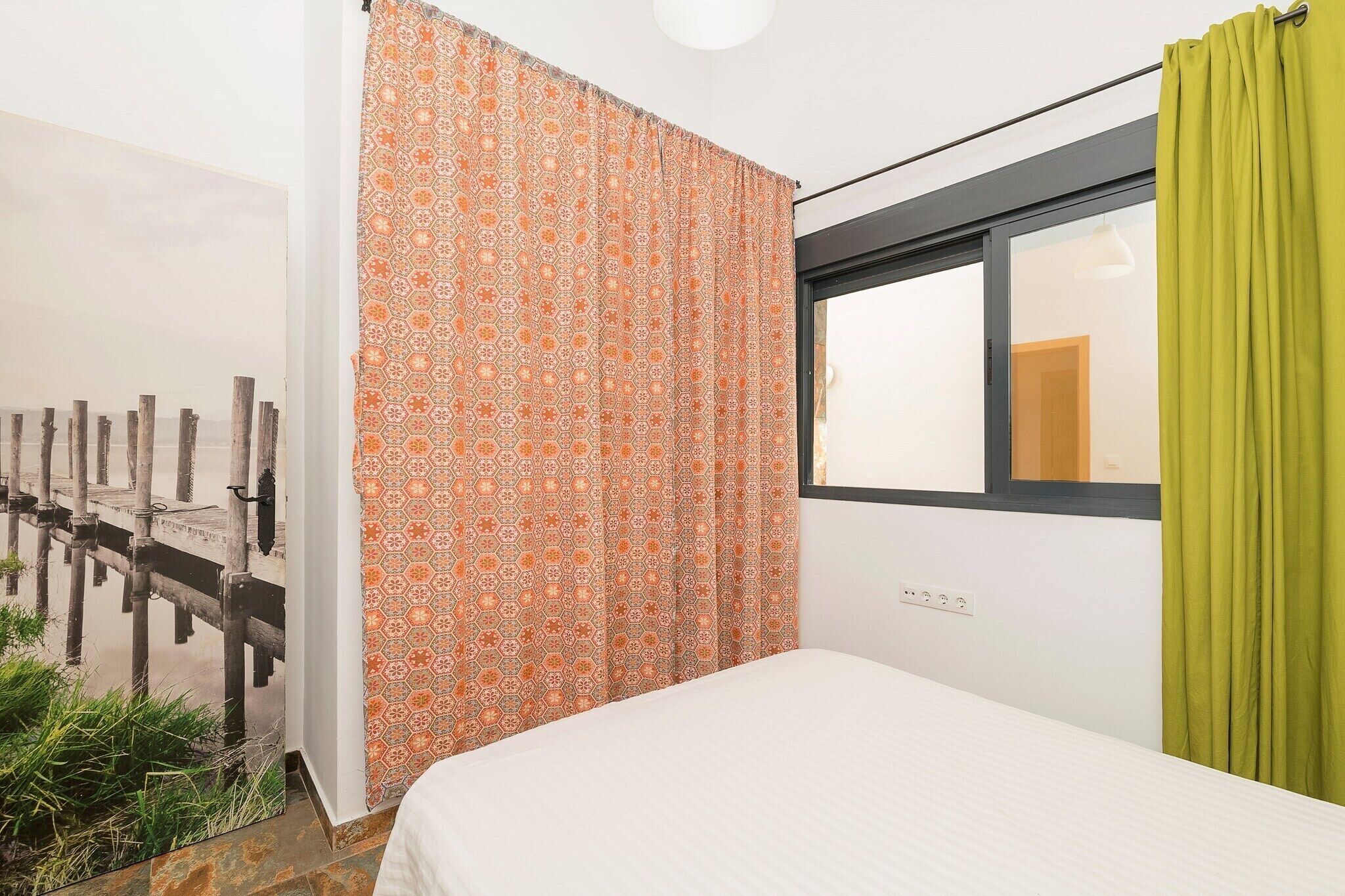 Une chambre à coucher avec un lit, une fenêtre donnant sur un quai en bois et des rideaux à motifs.