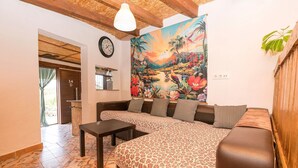 A living room with a sofa, a coffee table, a clock, and a large tropical mural on the wall. - Casa Amelie - Villa With Private Pool. Free Wifi (, Cádiz)