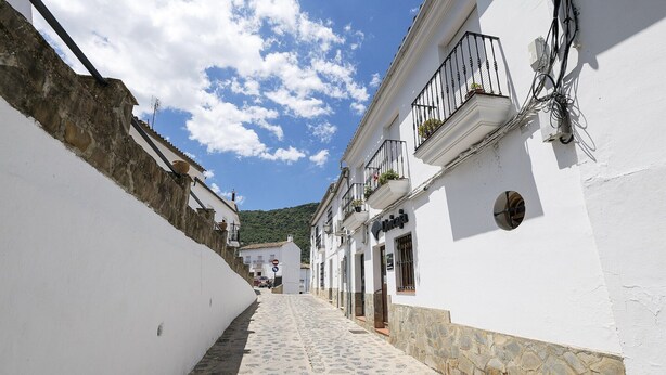 Une ruelle étroite pavée, bordée de bâtiments blancs dotés de soubassements en pierre et de balcons.