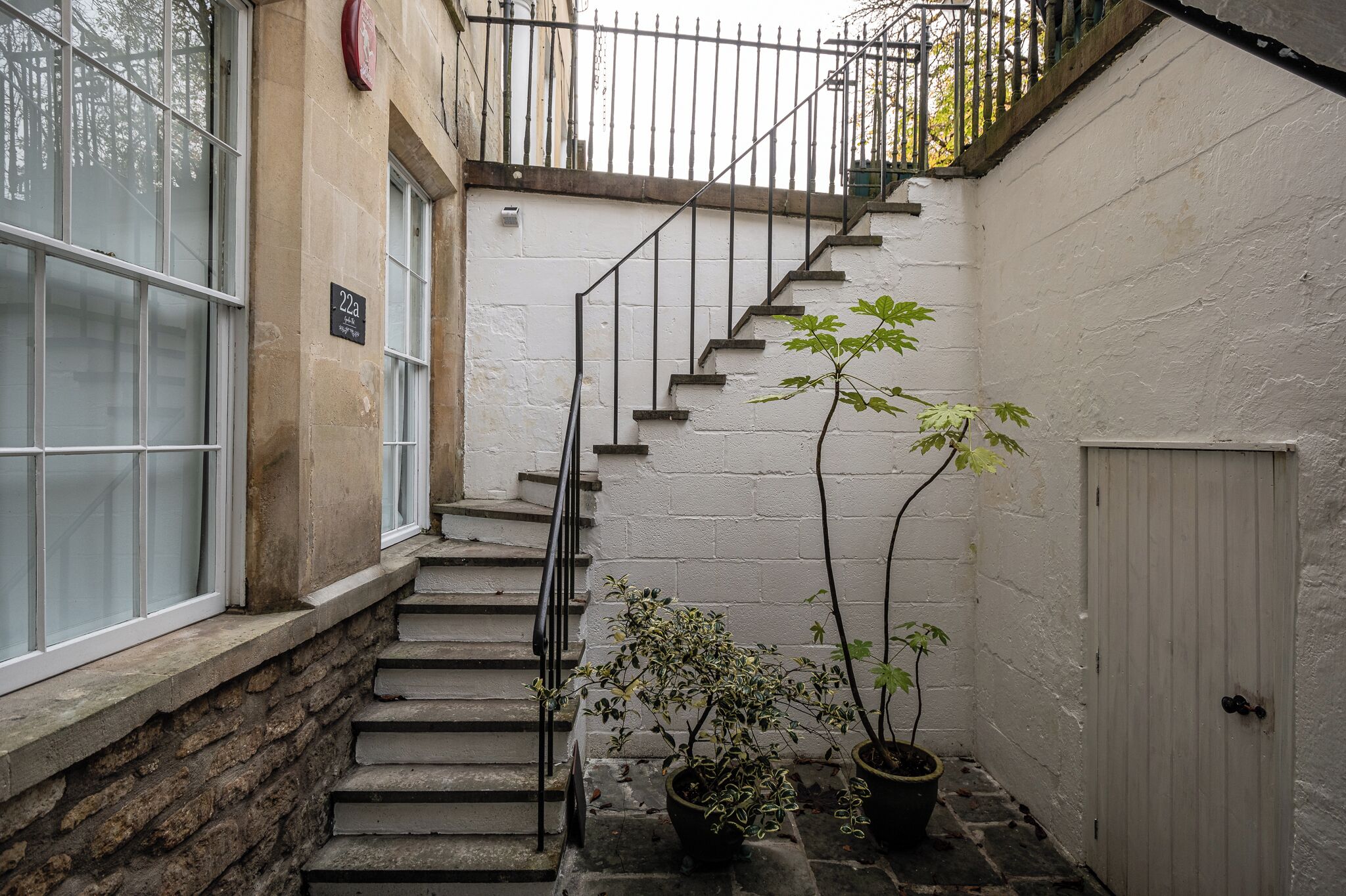 A narrow stairway with a metal railing, potted plants, and a white door.