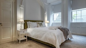 A bedroom with a large bed, two bedside tables, and a window with blinds. - Garden Flat Apartment in Grosvenor Place (Bath)
