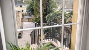A view from a window overlooking a courtyard with a stone wall, potted plants, and a metal railing. - Garden Flat Apartment in Grosvenor Place (Bath)