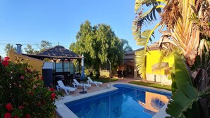 Ein Swimmingpool mit Liegestühlen, einem Gazebo mit Reetdach und üppiger Bepflanzung.