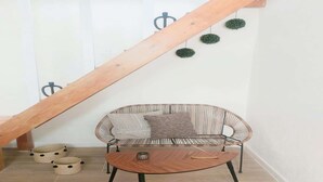 A room with a wooden staircase, a striped sofa, a round table, and two round baskets with black dots.