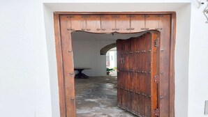 A wooden door with a decorative top and metal studs, leading into a building with a tiled floor and a visible archway in the background.