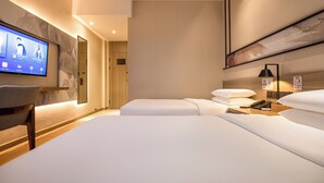 A modern hotel room with a large bed, a TV mounted on the wall, a bedside table with a lamp, and a wooden floor.