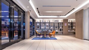 A modern hotel lobby with a reception desk, seating area, and shelves with decorative items.