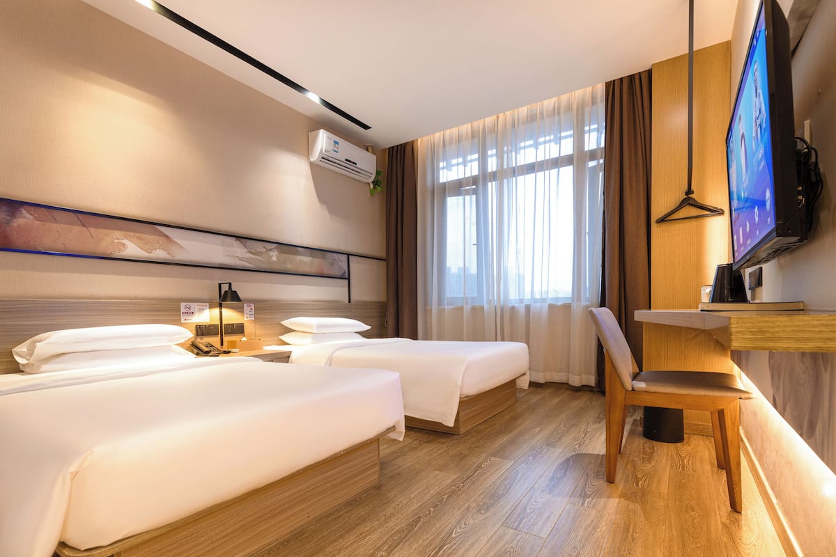 A hotel room with two beds, a desk with a chair, a TV, and a window with curtains.