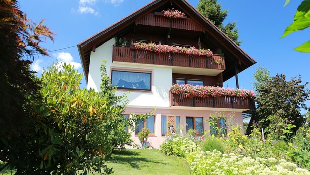 A two-story building with balconies, surrounded by greenery.