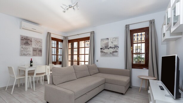 A modern living room with a beige sectional sofa, a dining table with chairs, a flat-screen TV, and a small side table. - Valleverde - Apartment In Mijas. Free Wifi (Mijas, Málaga)