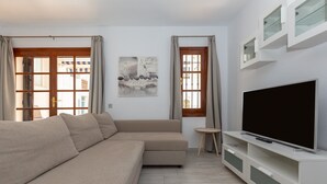A modern living room with a beige sectional sofa, a flat-screen TV on a white entertainment unit, and a small round side table. - Valleverde - Apartment In Mijas. Free Wifi (Mijas, Málaga)
