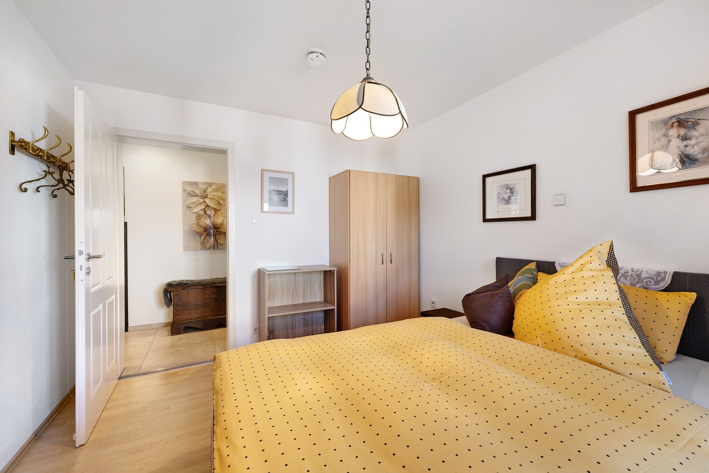 Une chambre à coucher comprenant un lit, une armoire, un luminaire suspendu et une porte donnant sur une autre pièce.