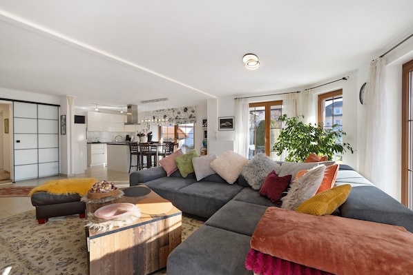 A modern living room with a sectional sofa, a wooden coffee table, and a dining area in the background.