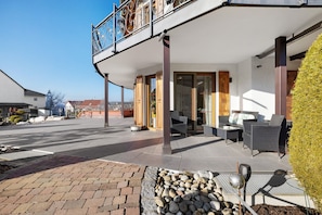 A modern building with a balcony, outdoor seating area, and a paved entrance.