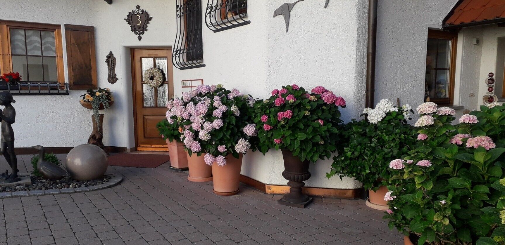 Une entrée d’immeuble avec une plaque numérotée, des éléments décoratifs sur le mur et des plantes en pot.