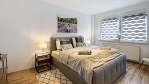 A bedroom with a bed, bedside tables, a window with blinds, and a painting on the wall.