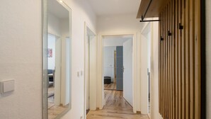 A hallway with wooden flooring, white walls, and a mirror on the left.