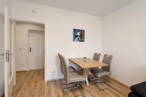 Una habitación con una mesa de comedor de madera, cuatro sillas, una planta pequeña en maceta y un cuadro de un perro en la pared.